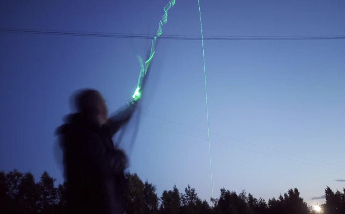 Archer's paradox in action Long-exposure photo of a glow-tipped arrow bending around the bow riser at release, tracing the archer's paradox flex path against a dusk sky