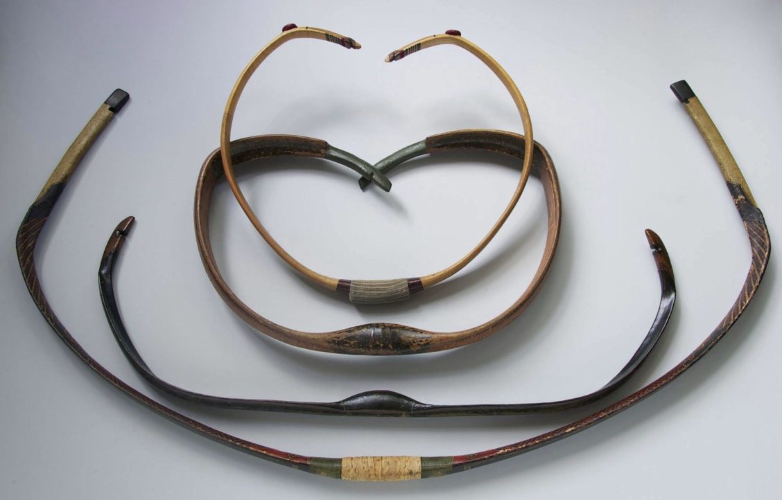 Unstrung Asiatic composite bows showing deep reflex Four unstrung Asiatic composite bows laid on a grey background, two curled almost into closed rings by their reflex and two long lacquered bows with dark angled siyah tips