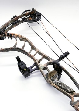 Close-up of a compound bow's dual-cam and cable system in a camouflage finish