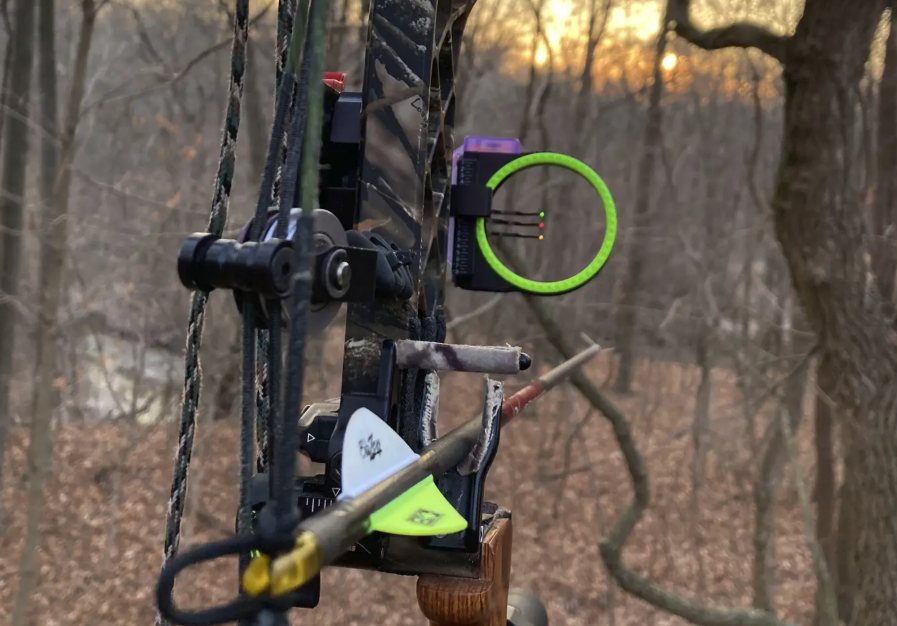 Compound bow sight pin and peep sight in low evening light in the woods, arrow nocked and ready