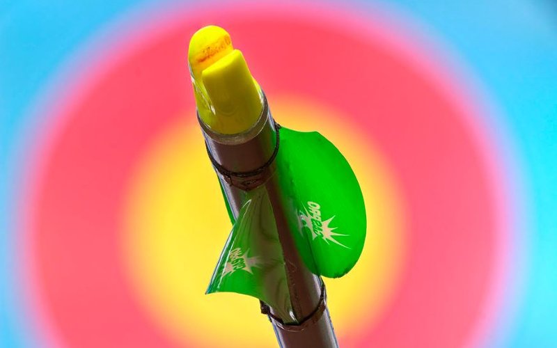 Feathers vs vanes aerodynamics comparison Bright green plastic vane fletching on an arrow shaft against a blurred archery target face โ feathers vs vanes aerodynamics comparison