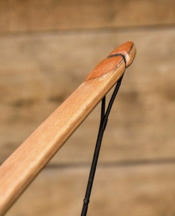 Close-up of a wooden bow limb tip with a shallow string groove, a small contrasting overlay and a black bowstring loop