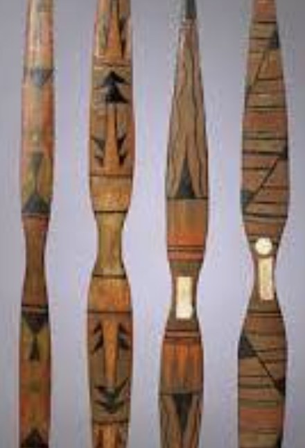 Four painted wooden bows standing side by side, each with broad flat limbs that narrow to a slim grip section