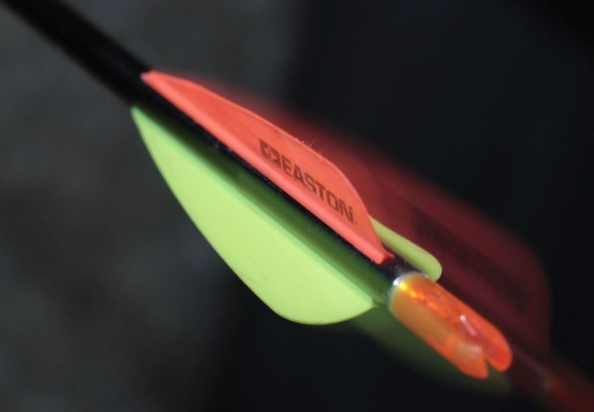Macro close-up of an orange and lime-green vane showing the twist angle clamped into the fletching
