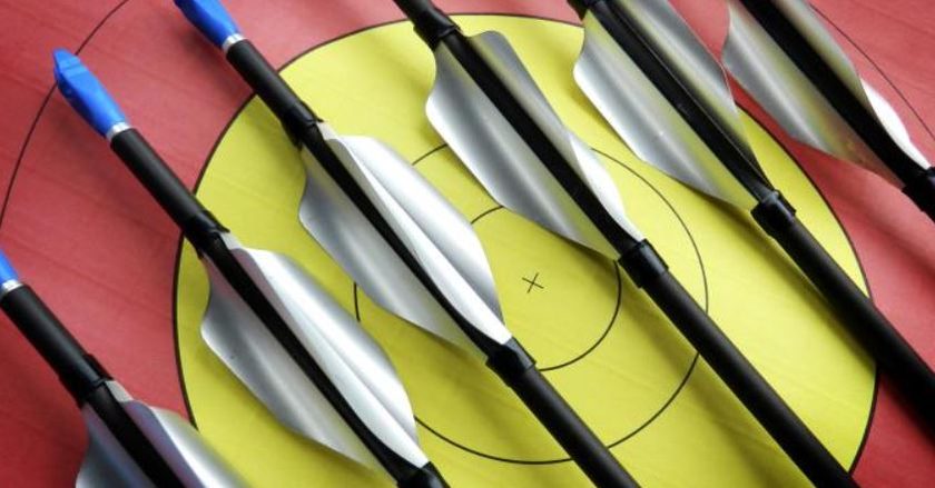 Tight group of helical-fletched arrows on a target face confirming clean clearance through the rest during testing