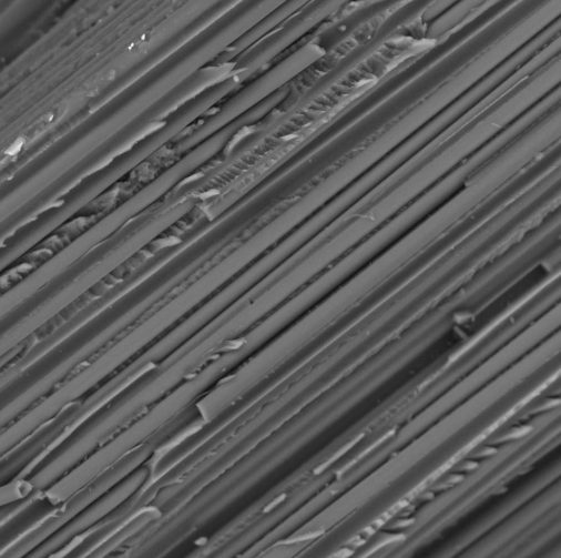 Macro close-up of dozens of parallel carbon fiber filaments running in tight, uniform bundles