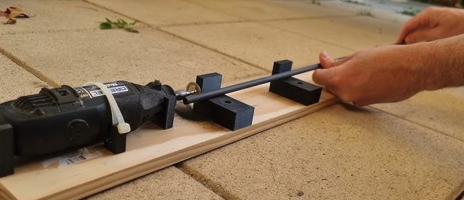 A carbon arrow shaft held in a shop-built wooden jig with support blocks, being cut with a rotary cutoff tool