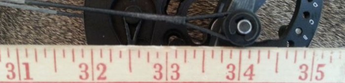 Close-up of a compound bow cam and cable system being checked against a tape measure during a press session