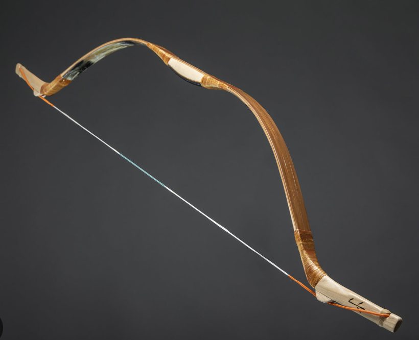 Braced Asiatic horn composite bow on a dark background: bark-wrapped limbs, dark horn showing on the belly near the grip, pale wooden siyahs angled forward at both tips and an orange-served string