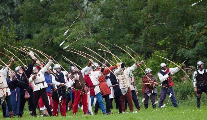 Reenactors in medieval dress firing a volley of arrows upward in formation with longbows