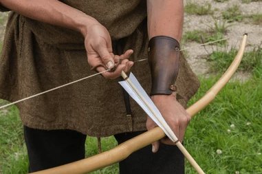 Close-up of an archer's fingers nocking an arrow on a recurve bow, wearing a leather forearm guard
