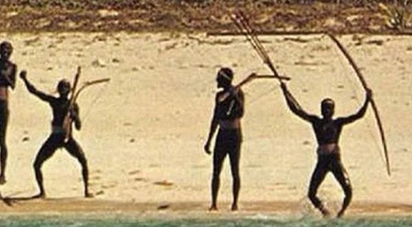 A group of traditional archers on a beach holding short hunting bows raised overhead