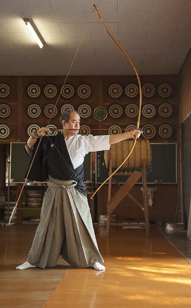 Yumi — modern kyudo full draw Modern kyudo practitioner at full draw with a Yumi in an indoor dojo