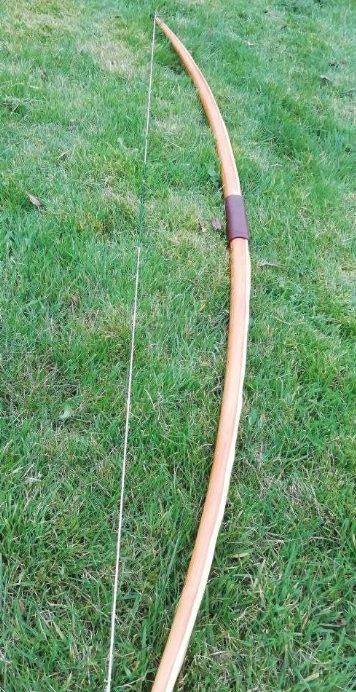 Self-bow stave — single-piece construction Strung self-bow resting on grass, showing the single continuous stave construction with no lamination