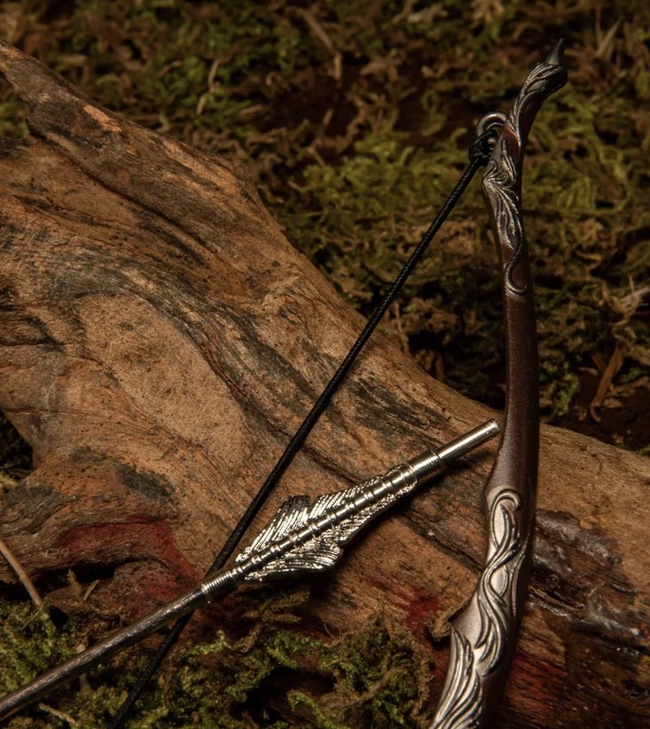 Ornate hand-carved wooden recurve bow with a decorative arrow, resting on a moss-covered log
