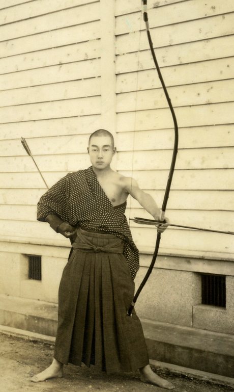 An early 20th-century Japanese archer in traditional dress at full draw with an asymmetric yumi bow