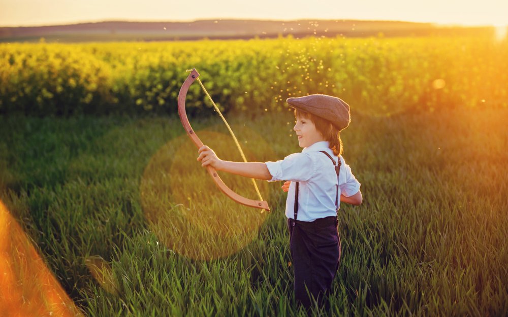 A young archer drawing a homemade bow in a golden wheat field at sunset