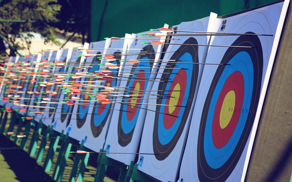 A row of official archery targets with arrows clustered tightly around the bullseyes