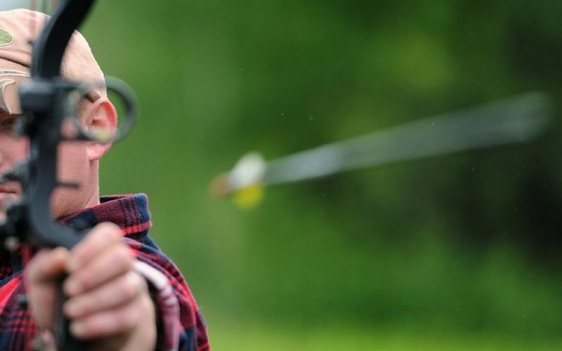 A compound bow archer at full draw with the arrow already in flight toward the target