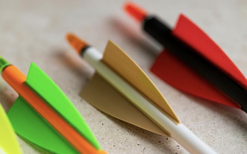 Arrow fletching types close up: green, tan and red plastic shield vanes on orange, white and black arrow shafts