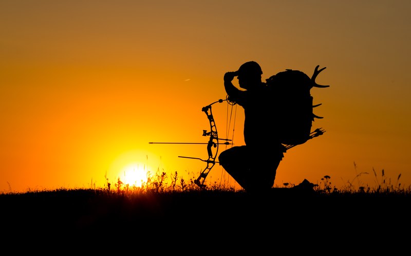 A hunter silhouetted at sunset carrying a pack and antlers