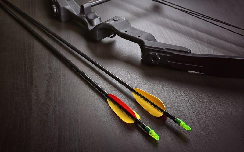 A compound bow with two fletched carbon arrows on a dark wood surface