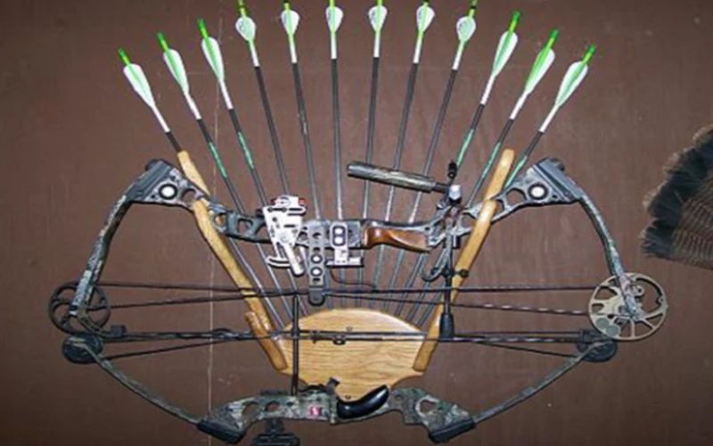 A camo compound bow mounted on a wall with arrows fanned above it